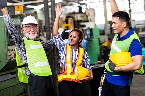 Two male and one female worker celebrate together in a manufacturing environment