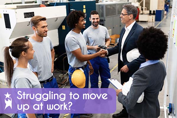 Diverse workers and managers in a production environment; two men shake hands, and workers wear blue pants, grey t-shirts, with some in yellow hard hats. A female manager holds a clipboard. Text on image says 'Struggling to move up at work?'