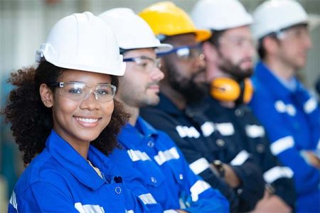 Diverse workers in blue coveralls and safety gear, representing temp-to-hire staffing for skilled roles.